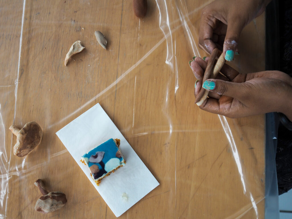 Zwei Hände formen und kneten Keramikpilze und ein Kuchenstück